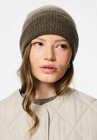 Gorro de punto acanalado marrón con un ajuste ceñido, combinado con una chaqueta ligera acolchada. Texturas destacadas incluyen lana suave y tela lisa.