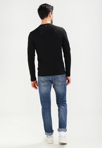 Czarna koszula z długim rękawem i okrągłym dekoltem, połączona z jasnoniebieskimi dżinsami i białymi trampkami. Szwy na koszuli i dżinsach.