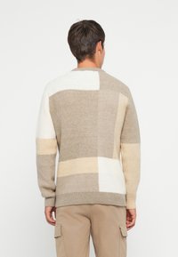 Μπεζ και κρεμ χρώμα-μπλοκαρισμένος σκούφος με στρογγυλή λαιμόκοψη, κατασκευασμένος από μαλακό πλεκτό ύφασμα. Διαθέτει διάφορα σχήματα και ριγέ στριφώματα.