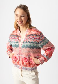 Färgglad zip-up bomberjacka med intrikata geometriska mönster i rosa, röd, grön och blå. Ribbad manschetter och nederkant ger textur.