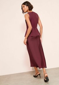 Bordó peplum felső testhezálló szabással, hozzáillő hosszú szoknyával párosítva. Sima anyagból, ujjatlan kialakításban, elegáns fekete magas sarkú cipőkkel.