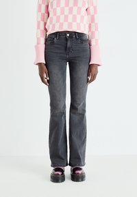 Vaqueros acampanados grises con una cintura de altura media, combinados con un suéter a cuadros en tonos rosa y crema y zapatos de plataforma negros gruesos.