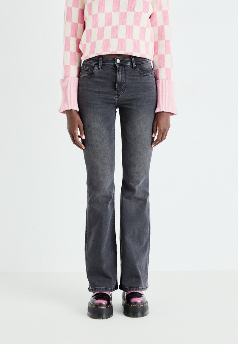 Vaqueros acampanados grises con una cintura de altura media, combinados con un suéter a cuadros en tonos rosa y crema y zapatos de plataforma negros gruesos.