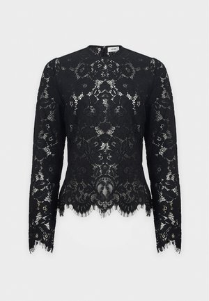 Mujer con un top largo de encaje negro con una camiseta negra debajo, combinado con una falda larga negra de cintura alta y tacones negros.