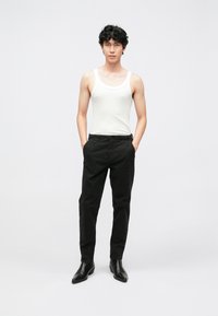 White tank top, black trousers, and black shoes. The trousers have a smooth texture with a slim-fit design. Overall, a simple, casual outfit.