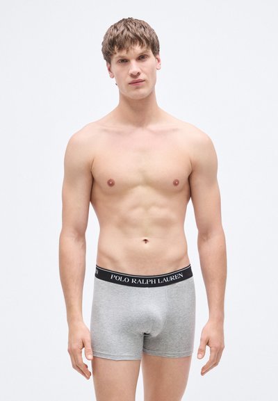 Grå bomullsboxere med svart elastisk midjebånd med preget tekst "POLO RALPH LAUREN." Modellen poserer forfra med naken overkropp.