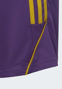 Lila Sporttrikot mit gelben Streifen, das ein strukturiertes Panel und einen gestickten Saum aufweist, entworfen für Komfort und Flexibilität in der Bewegung.