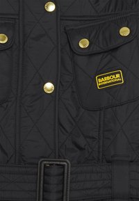 Černá prošívaná bunda s zlat�ými patentkami, dvěma náprsními kapsami a opaskem v pase s obdélníkovou sponou. Na viditelném místě je štítek "Barbour International".