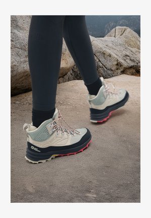 Lightweight hiking shoes with a beige upper, mesh and leather materials, gray accents, pink and black rubber sole, and patterned laces.