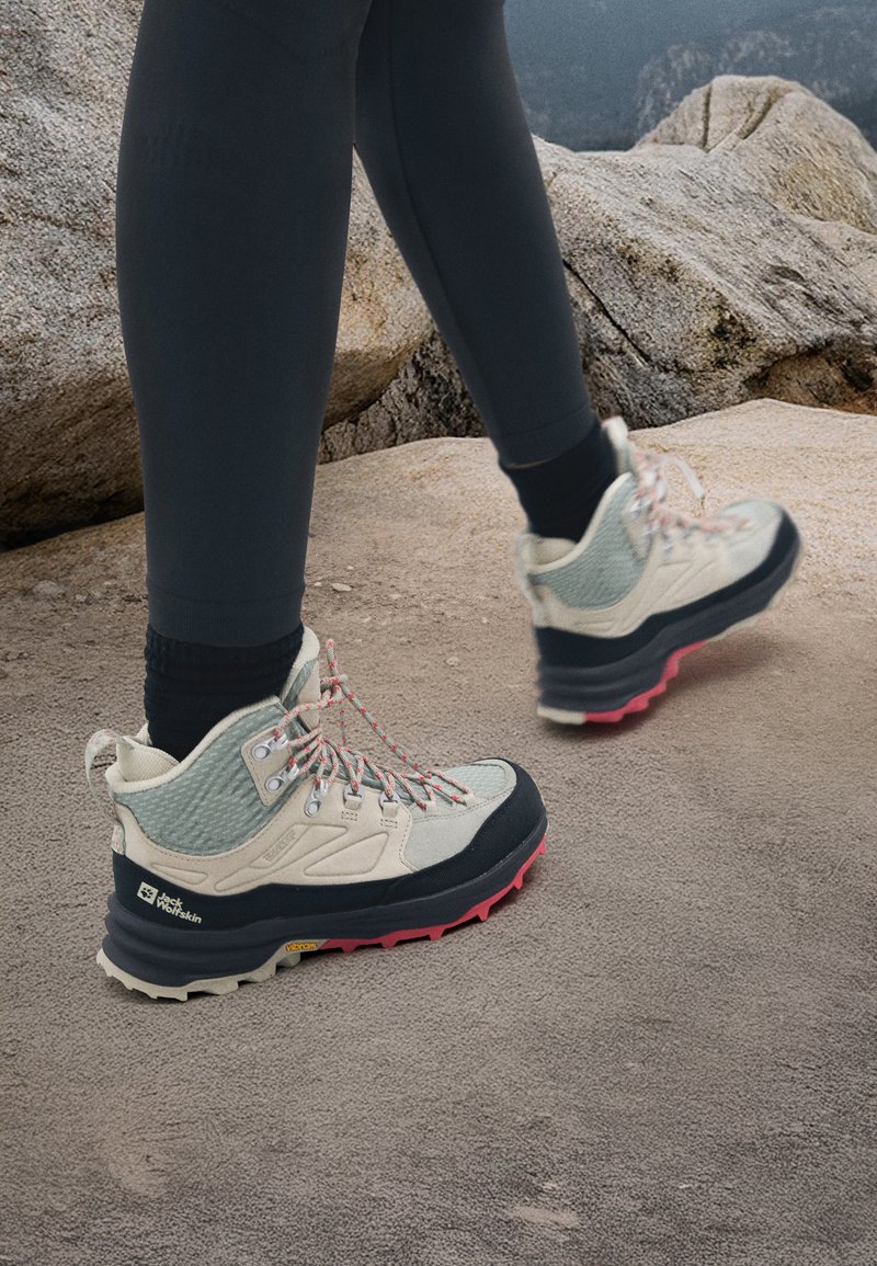 Leichte Wanderschuhe mit einem beigen Obermaterial aus Mesh und Leder, grauen Akzenten, pinkem und schwarzem Gummi sohle und gemusterten Schnürsenkeln.