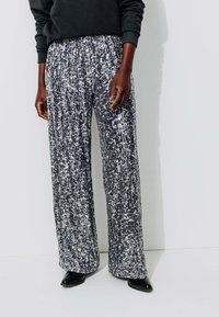 Pantalons larges en tissu sequiné noir et blanc avec un motif texturé, dotés d'une taille élastique et d'une silhouette lâche et fluide.