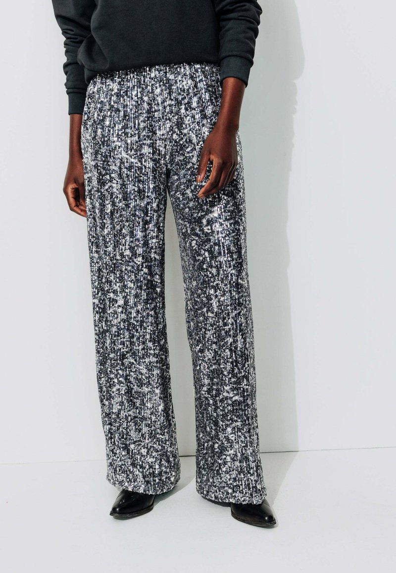 Pantalons larges en tissu sequiné noir et blanc avec un motif texturé, dotés d'une taille élastique et d'une silhouette lâche et fluide.