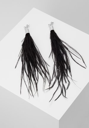 Paire de longues boucles d'oreilles à pompons en plumes noires avec tiges en argent, présentées sur une surface blanche inclinée.