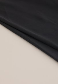 Črn material z gladko teksturo, urejeno zložen na bež površini. Material se zdi lahkoten in prilagodljiv.