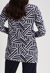 Marinblus med ett geometriskt mönster av vita ränder och former, lång ärm och avslappnad passform, tillverkad av ett lätt material.