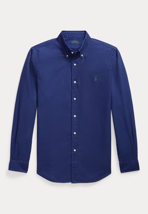 Chemise boutonnée bleu foncé en coton, à manches longues, avec un col évasé et un petit logo vert sur la poitrine gauche.