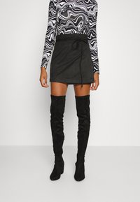 Černá semišová zavinovací sukně s páskem v pase, doplněná černými texturovanými kozačkami nad kolena. Dlouhý rukáv topu zdobí vlnitý černo-bílý vzor.