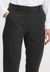 Donkergrijze op maat gemaakte broek van textuurstof, met zijzakken en een standaard tailleband, gecombineerd met een witte langslavende shirt.
