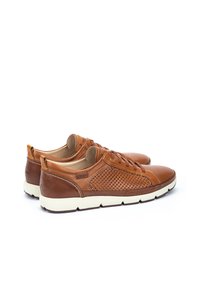 Zapatos de cuero marrón con un diseño perforado en los lados, suela de goma color crema y cordones en la parte delantera. Punta redondeada.