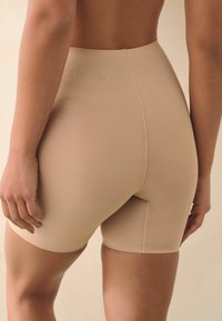 Shorts beige modellanti, lunghezza a metà coscia, texture liscia, vita elastica, cuciture minime, design aderente, che offrono supporto e copertura.