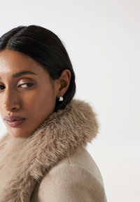 Manteau beige avec un col en fausse fourrure douce et de couleur claire. Texture de tissu lisse, complétant la palette de couleurs douce et atténuée.
