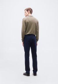 Πράσινο χακί μακρυμάνικο πόλο και παντελόνι σκούρο ναυτικό με ίσια γραμμή στα πόδια. Απλός σχεδιασμός χωρίς ορατά σχέδια ή διακοσμητικά στοιχεία.