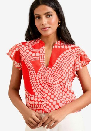 Blusa rossa con maniche corte a volant, con un motivo a pois circolari di diverse dimensioni e scollatura a V. Bottoni lungo la parte anteriore.