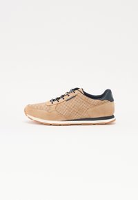 Baskets en suede beige avec un design perforé, accents noirs, semelle intermédiaire blanche et fermeture à lacets. Présente une semelle extérieure en caoutchouc texturé.
