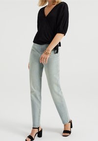 Czarna, teksturowana bluzka z krótkimi rękawami, zestawiona z jasnoniebieskimi jeansami o prostym kroju i czarnymi sandałami na wysokim obcasie. Złota bransoletka na nadgarstku.