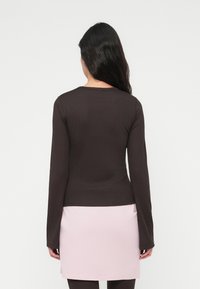 Καφέ ριμπ μακρυμάνικη μπλούζα με στρογγυλή λαιμόκοψη, συνδυασμένη με φούστα ανοιχτού ροζ χρώματος. Λεπτή υφή, εφαρμοστή σχεδίαση.