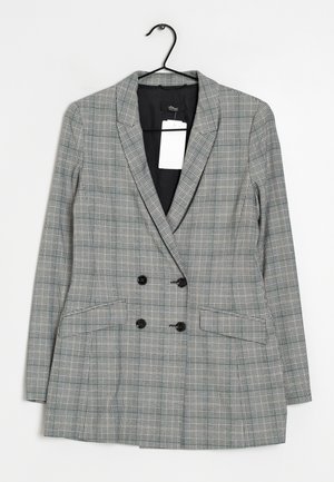 Blazer de cuadros gris con doble botonadura, botones negros, solapas y bolsillos delanteros, colgado en una percha negra con una etiqueta blanca.