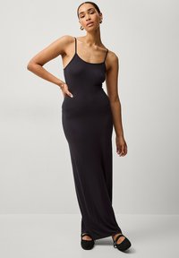 Schwarzes Maxikleid mit dünnen Trägern, figurbetont und mit glatter Textur. Entworfen mit einer langen Silhouette und einem seitlichen Schlitz am Saum.