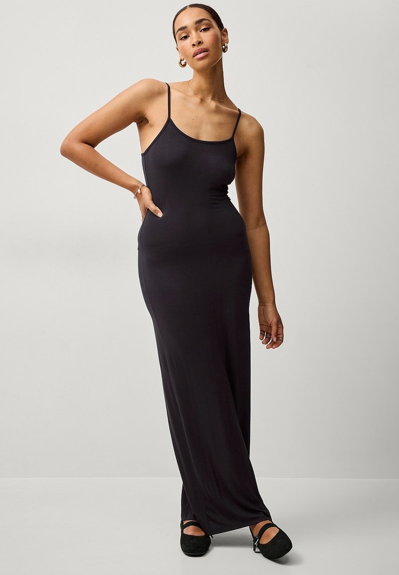 Schwarzes Maxikleid mit dünnen Trägern, figurbetont und mit glatter Textur. Entworfen mit einer langen Silhouette und einem seitlichen Schlitz am Saum.