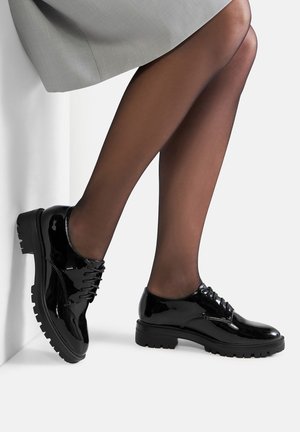 Fekete lakkbőr fűzős cipők vastag gumitalppal, sima felülettel, kerek orral és díszes fűzőkkel.