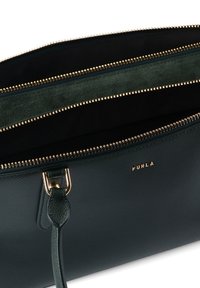 Πράσινη τσάντα χειρός από υφή δέρματος με χρυσά μεταλλικά στοιχεία, που διαθέτει τρεις θήκες με επένδυση από σκούρο ύφασμα και εμφανές λογότυπο της μάρκας.