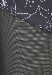 Tekstilet har en øverste del med et kosmisk stjernemønster på en mørk bakgrunn og en nederste del i et strukturert, ensfarget svart materiale.