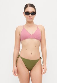 Ružičasti bikini gornji dio s tankim trakama, uparen s maslinastozelenim donjim dijelom bikinija s bočnim vezicama. Glatka tekstura, minimalistički dizajn.