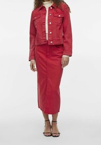 Rød denimjakke med forlommer, knaplukning og matchende rød blyantskjørt. Model iført sorte sandaler med stropper. Glat tekstur.