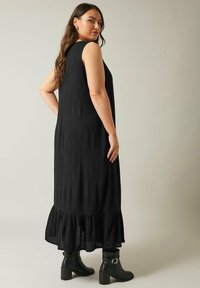 Vestido maxi sin mangas negro con tejido texturizado, que presenta un dobladillo con volantes en capas. Combinado con botines negros de tobillo con tacón cuadrado.