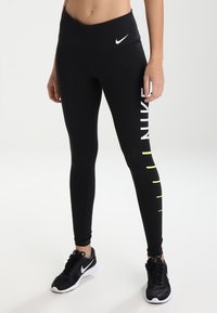 Leggings neri con vita alta, caratterizzati da testo bianco "NIKE" e accenti neon sul lato, progettati per uso atletico.