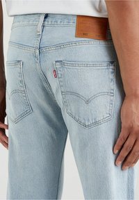 Jeans de denim azul claro con una textura desgastada, que cuentan con dos bolsillos traseros y un parche de cuero en la cinturilla con los detalles de la marca.