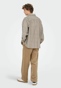 Gegolfde, bruine en beige shirt met lange mouwen en een opgevouwen kraag, gecombineerd met tan corduroy broek en witte sneakers.