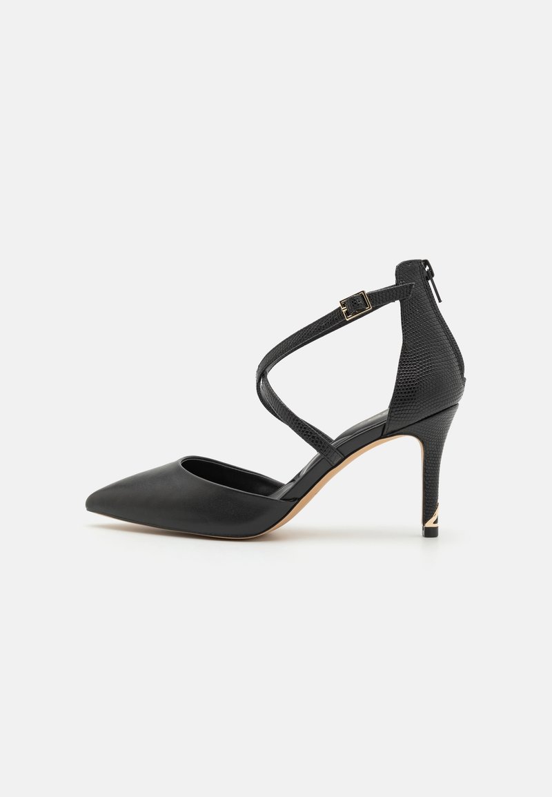 Chaussure noire à talons hauts avec un bout pointu, une sangle de cheville texturée traversant le pied, une boucle et une fermeture éclair à l'arrière.