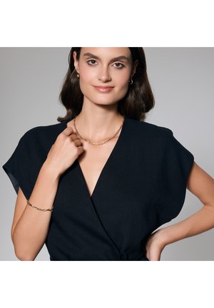 Czarna bluzka z dekoltem w serek i krótkimi rękawami; model nosi złoty naszyjnik oraz bransoletkę, eksponując gładkie faktury i nowoczesny design.