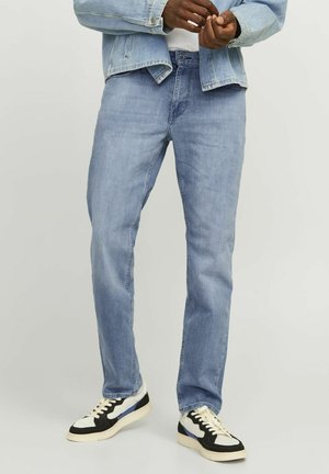 Jeans de mezclilla azul claro con corte recto, que cuentan con un diseño de cinco bolsillos. Combinados con zapatillas negras y blancas.