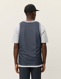 Fekete és kék csíkozott kosárlabda mez egy szürke rövid ujjú póló fölött, texturált fekete sapkával kombinálva, hátulról nézve.