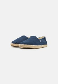 Scarpe slip-on in tessuto blu navy con punta arrotondata, suola in juta e dettagli cuciti sulla parte superiore. Accentuate da una piccola etichetta con logo.