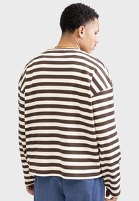 Bruine en crèmekleurige gestreepte langearmshirt van een gestructureerd, ribbelachtig materiaal. Kenmerkt zich door een relaxte pasvorm en een ruime ronde hals.