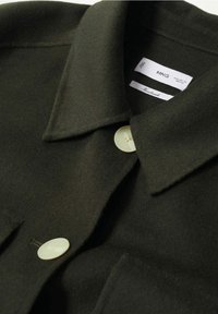 Chaqueta de lana verde oscuro con un gran cuello, dos botones y una tela suave y texturada. Las etiquetas indican "MNG" y "Hecho a mano."