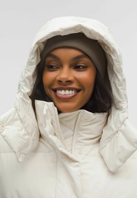 Kohvivahetav kreemika v�ärviga paks jakk, millel on kõrge krae ja suur kapuuts, varustatud tõmbluku ja nööpide aksessuaaridega. Kandmine pruunist kudumist beebiga.